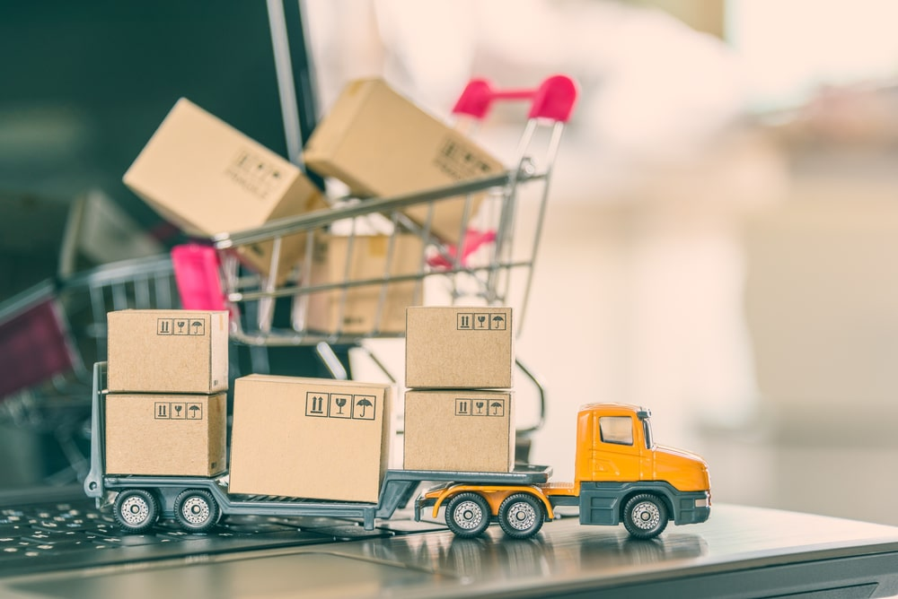A toy truck carrying small boxes with a small trolley at the back on top of a laptop