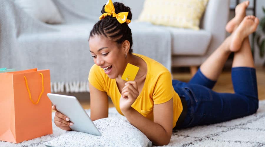 A female online shopper using her table while holding up her card.