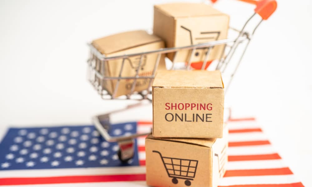 A miniature shopping cart with shipping boxes on top of an American flag