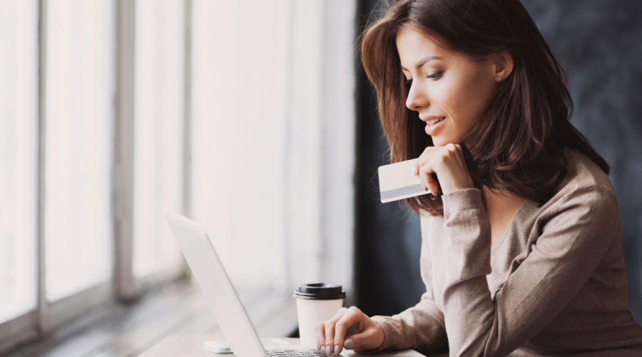 A woman holding her credit card while scrolling through her laptop.