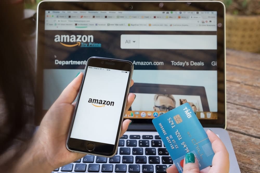 A person holding a credit card browsing Amazon on mobile and laptop computer.